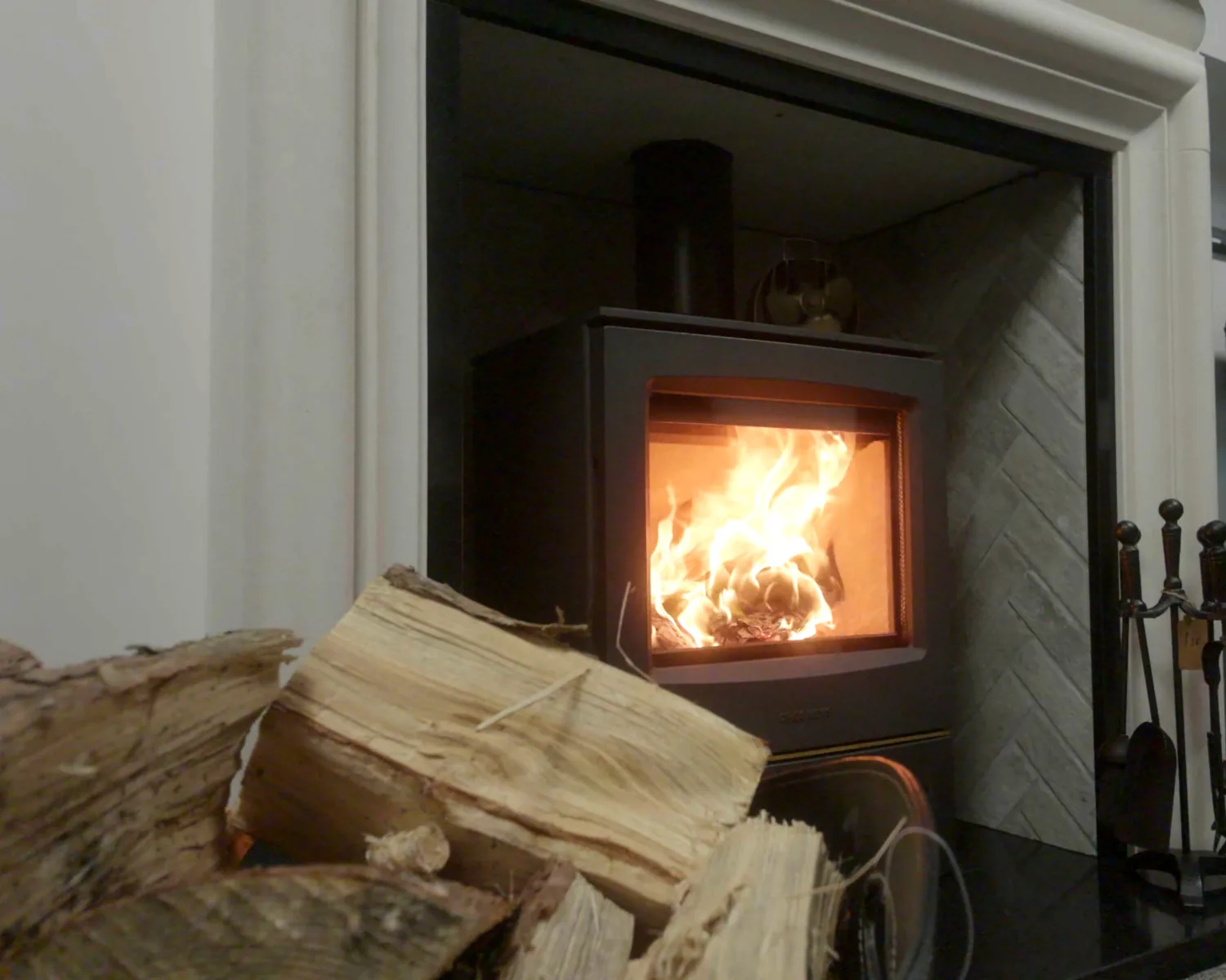 A lit stove beside a basket of logs in the Fife Stoves showroom